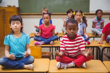 Pupils meditating in lotus position on desk in classroom