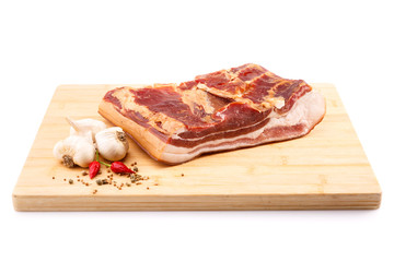 Piece of bacon with garlic and red pepper on wooden board