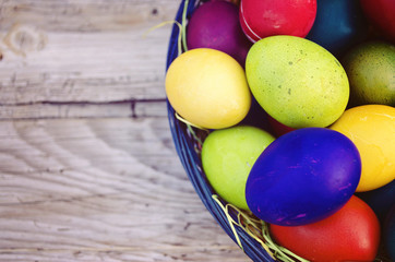 Colorful Easter eggs in basket on wooden background