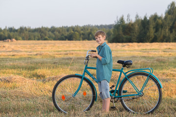 Fototapeta premium Smiling teenager boy holding bicycle in farm field