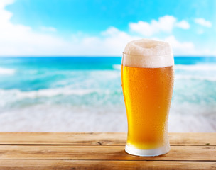 glass of beer on wooden table over sea