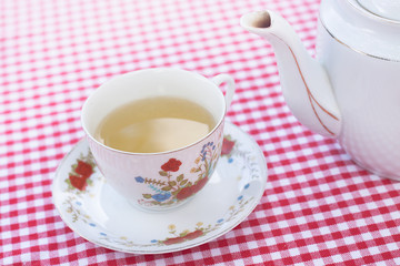 teapot and cup with tea on checkerboard background