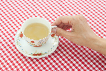 female hand holding a cup of tea on checkerboard background