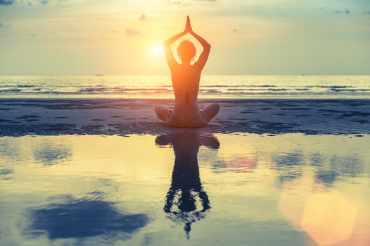 Young female practicing yoga on the beach at amazing sunset.
