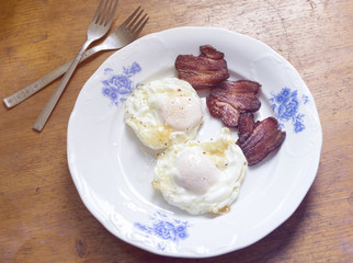 Breakfast plate with eggs and bacon on wooden table