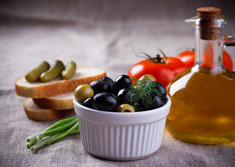 Olives in white bowl and  bottle of olive oil on jute fabric