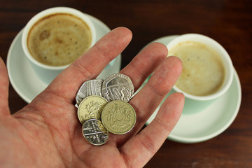 English Currency in hand with two coffee  in background.