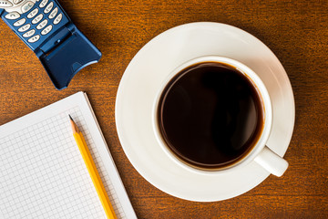 Cell phone and cup of the coffee on the wooden table with a note