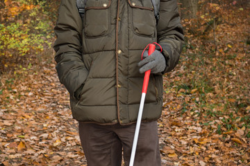 Blind person holding a stick and walking in the forest park