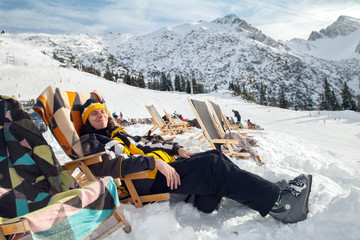 Man sits on sun-lounger in alpian ski resort - 76871103