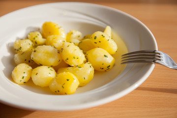 The white plate of boiled potatoes with spices on table