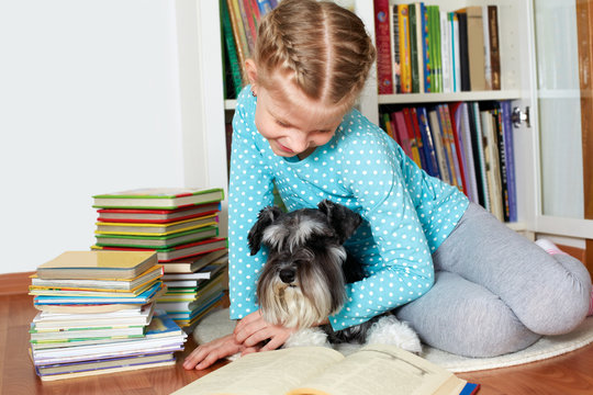 girl and her dog in glasses reading a book, sitting on floor in