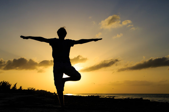 Silhouette of young man doing yoga at sunset