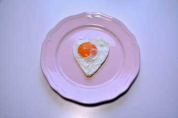Heart shaped egg on a a pink plate.