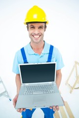Happy repairman wearing hard hat while holding laptop