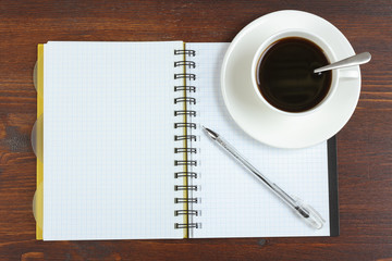 Cup of coffee, pen and opened notepad on desk. Top view