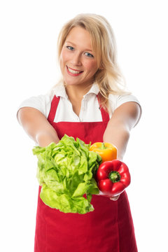 Frau mit Schürze präsentiert einen Salatkopf und Paprikas