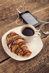 Having coffee and croissants with smartphone and headphones