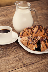 Breakfast with coffee, milk and croissants on wooden table