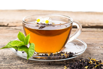Glass Cup Tea with camomile flower and Mint Leaf, on brown woode