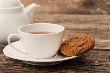 ivory tea cup with sweet cookie, and kettle on wooden palette
