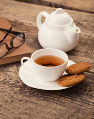 ivory tea cup with sweet cookie, glasses and book on wooden pale