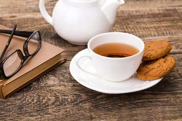 ivory tea cup with sweet cookie, glasses and book on wooden pale