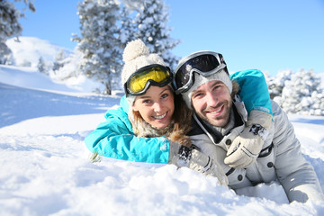 Cheerful couple of skiers laying down in snow