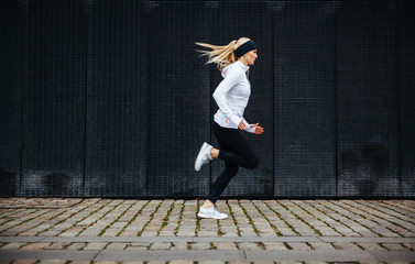 Sporty young woman running on sidewalk in morning