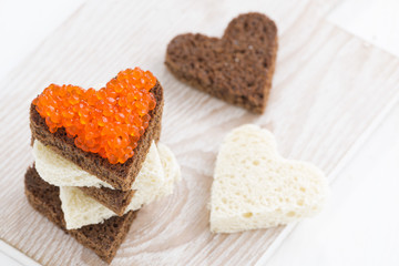 Fototapeta na wymiar toasts with red caviar in heart shape on wooden board