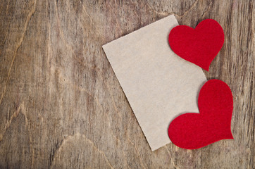 Two Red fabric hearts with sheet of paper on old wooden table
