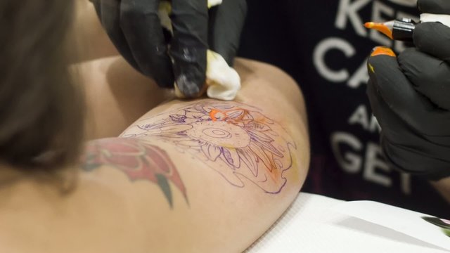 Artist tattoing a flower on girls shoulder
