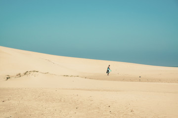 Fototapeta na wymiar Bright sand dunes with female tourist walking to the horizon. Cl