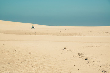 Bright sand dunes with female tourist walking to the horizon. Cl