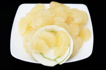 Peeled sweet green grapefruit on a white dish against black back