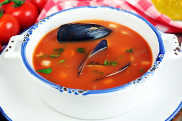 Tasty soup with mussels, tomatoes and black olives in bowl