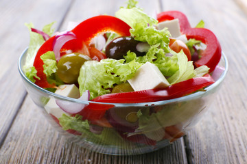 Greek salad in glass dish on wooden table background