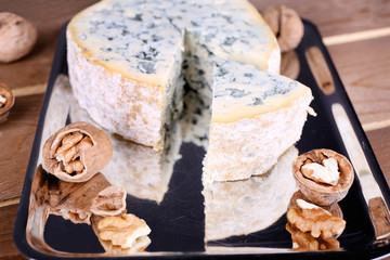 Blue cheese with nuts on metal tray and wooden table background