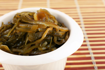 Seaweed in white bowl on bamboo mat background