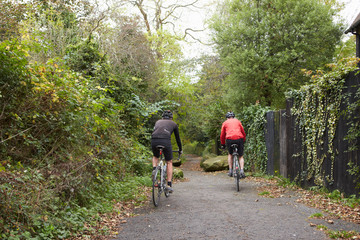 Two Mature Male Cyclists Riding Bikes Along Path