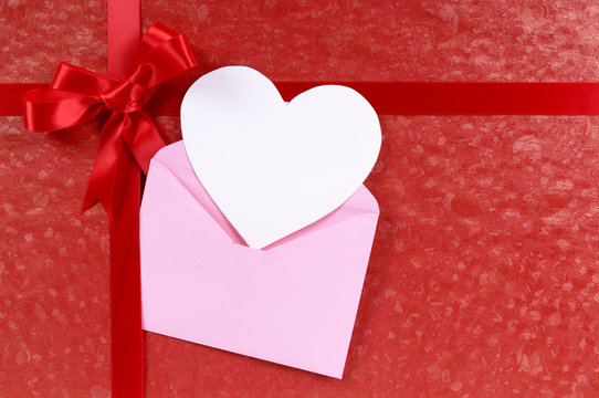 Valentine gift present with pink envelope red ribbon paper background and blank message card or tag valentines day photo