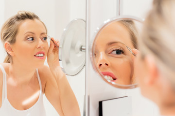 Young woman tweezing eyebrows in bathroom