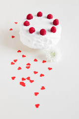 White cake with raspberries and red hearts on white background