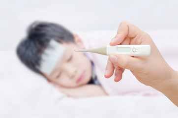 Mother holding digital thermometer and sick little boy in bed