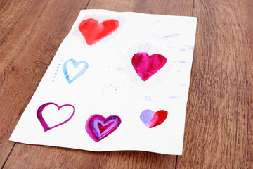 Painted hearts on sheet of paper on wooden table background