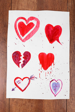 Painted hearts on sheet of paper on wooden table background