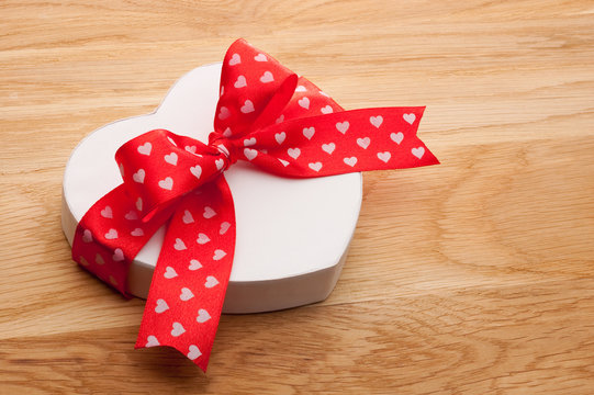 Gift in the form of heart tied with red ribbon with a bow on woo