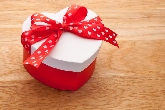 Gift in the form of heart tied with red ribbon with a bow on woo