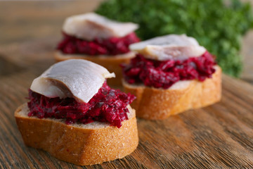 Herring with beets on rye toasts on wooden background