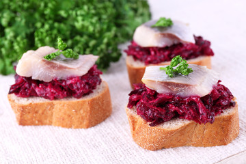 Rye toasts with herring and beets on tablecloth background